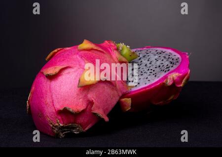 Fruit Pitaya ou Dragon à chair blanche avec la coquille externe à échelle au premier plan montrant de la pulpe blanche avec des graines noires incrustées sur une surface noire Banque D'Images