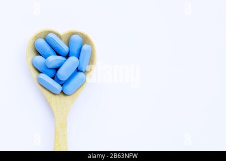 Pilules médicales bleues avec cuillère en bois en forme de coeur sur fond blanc. Espace de copie Banque D'Images