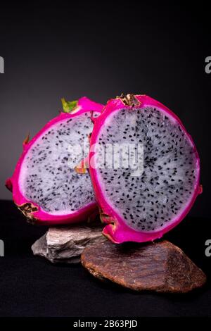 A ouvert des fruits Pitaya ou Dragon à chair blanche exposés sur deux roches avec la peau extérieure et aussi de la pulpe blanche avec des graines noires incrustées Banque D'Images