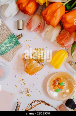 Commission d'humeur du printemps pour femme. Un bouquet de tulipes lumineuses de différentes couleurs, des suites débordant d'une petite coupe d'or, du parfum, du livre, du rouge à lèvres et du rif Banque D'Images