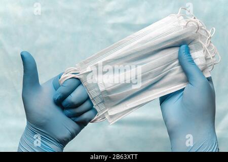 Le médecin tenant le masque médical de lot dans les mains en gants médicaux bleus et montrant le pouce vers le haut. Assurance en cas de pandémie, grippe, maladies aéroportées, SRAS Banque D'Images