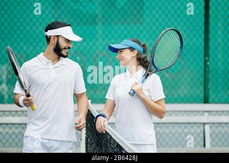 Joyeux couple en uniforme blanc à jouer au tennis ensemble Banque D'Images