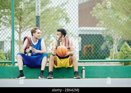Heureux jeunes sportifs se raser de pause, l'eau potable et discuter de jeu après avoir joué au basket-ball à l'extérieur Banque D'Images