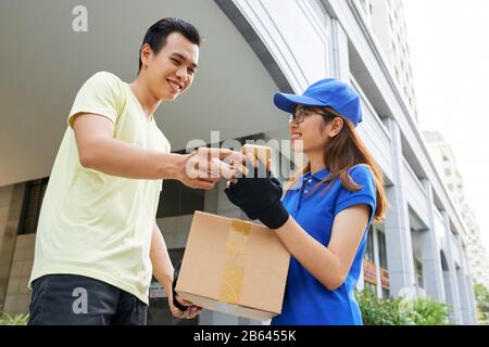 Une jeune femme souriante qui donne un paquet et demande au client de signer un document sur son smartphone Banque D'Images