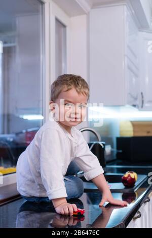 Portrait de joyeux beau garçon dans l'arrière-plan de la cuisine. L'enfant mange une pomme, roule une voiture jouet sur la table et aime la vie. Heureux et insouciant enfance. Concept de saine alimentation. Banque D'Images