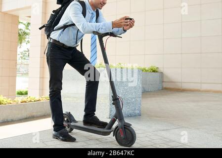 Image recadrée d'un entrepreneur positif qui vérifie l'application de carte sur son smartphone avant de monter sur un scooter électrique Banque D'Images