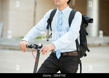 Image recadrée de jeune homme d'affaires avec grand sac à dos à cheval scooter électrique de kick Banque D'Images