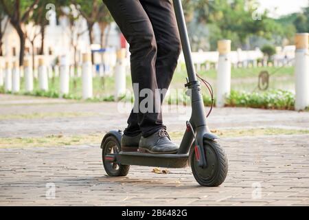 Image courte de jeune homme d'affaires qui monte sur un scooter électrique de kick dans le parc de la ville et qui se fait mal au travail Banque D'Images