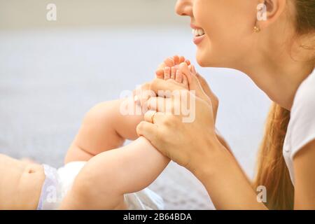 La mère heureuse embrasse les pieds du bébé Banque D'Images