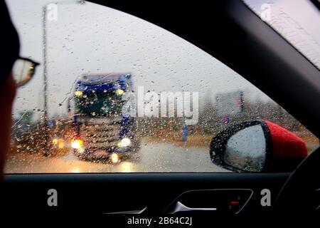 Conduite sur route sous de fortes pluies, conducteur regardant la circulation qui s'entrecroise avec un camion qui attend d'entrer dans la route. Banque D'Images