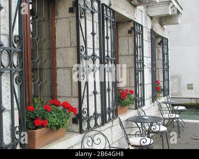 Tables et chaises vides dans un café extérieur décoré de fleurs rouges dans des boîtes à fenêtre Venise Italie. Banque D'Images