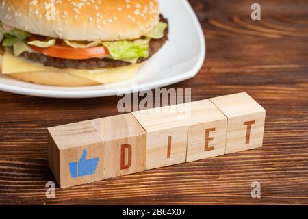 Blocs avec comme dans la forme d'une main et le mot régime à côté d'un hamburger sur un fond en bois. Gros plan. Banque D'Images