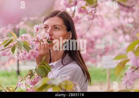 Une jeune fille caucasienne aime l'arôme et la beauté des cerisiers en fleurs. Cerisiers en fleurs dans le parc municipal de Dnipro Ukraine en Europe de l'est. Banque D'Images