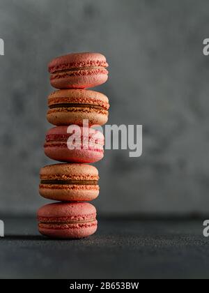 Pile de macarons français parfaits. Rangée verticale de macarons de pêche et de rose sur fond gris texturé, espace de copie à droite. Vertical Banque D'Images