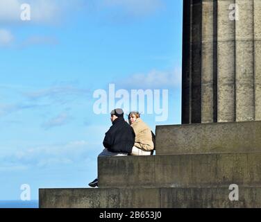 Jeune couple assis sur des marches à Carlton Hill, Édimbourg, en profitant de la vue. Ciel bleu et nuages. Banque D'Images