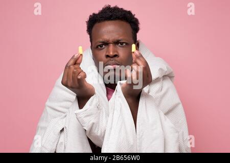 Les bouchons d'oreille de youngman afro-américains agacés se réjouirent de la solution de voisins bruyants qui veulent dormir. Notion d'insomnie sur le mur rose. Banque D'Images