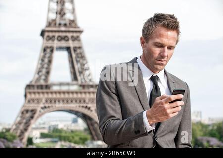 Homme d'affaires européen sérieux se tenant à l'extérieur en utilisant son téléphone portable devant la Tour Eiffel à Paris, France Banque D'Images