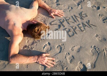 Un jeune dude est passé sur la plage à côté du message Spring Break dans le sable d'empreinte Banque D'Images