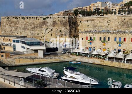 Les cafés et Les Restaurants bordent le front de mer de la Valette sous les remparts fortifiés en face d'une petite marina. Banque D'Images