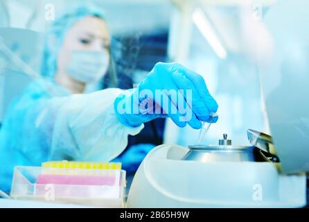 Une scientifique féminine dans un masque médical de protection et des gants en caoutchouc fait des tests d'ADN PCR dans un laboratoire chimique et bactériologique moderne. Banque D'Images