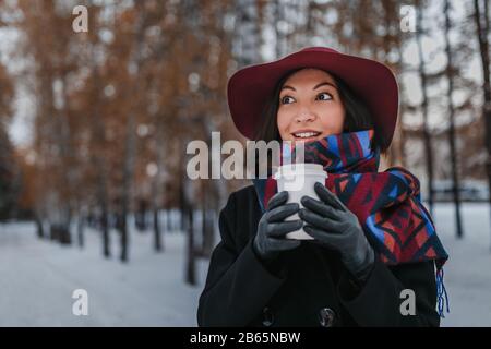 Femme avec grande tasse de boisson chaude à emporter pendant la journée froide. Habillée d'un chapeau à large bord et d'un foulard brillant Banque D'Images