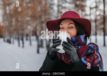 Femme avec grande tasse de boisson chaude à emporter pendant la journée froide. Habillée d'un chapeau à large bord et d'un foulard brillant Banque D'Images