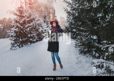 Fille en manteau et chapeau avec café à emporter marchant sur le chemin d'hiver entre les rangées d'arbres. Banque D'Images