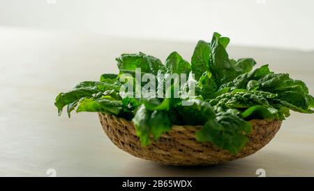 Concept de nourriture végétalienne saine : rétroéclairage de gros plan avec effet bokeh de feuilles d'épinards verts fraîchement cueillies placées dans un panier en osier sur une ta en bois blanc Banque D'Images