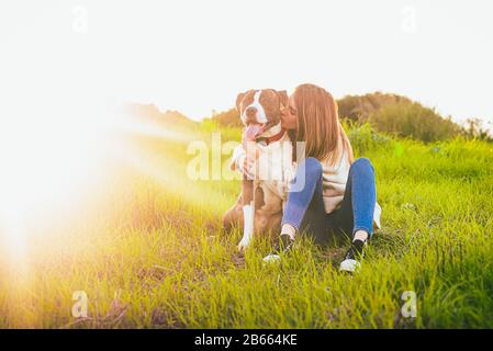 Jeune femme béatie qui embrasse le chien sur le terrain. Terrier américain du Staffordshire Banque D'Images