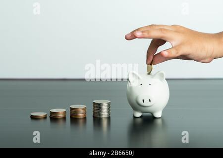 Concept d'économie d'argent et de don, l'enfant met de l'argent sur la jolie banque de porc blanc Banque D'Images