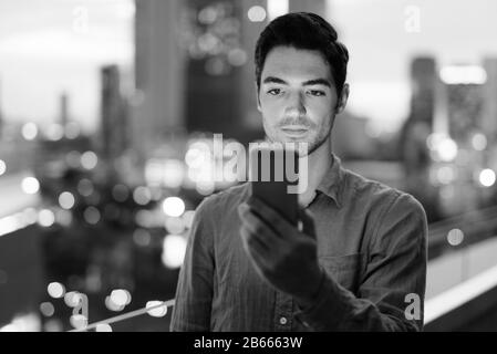 Jeune homme d'affaires utilisant le téléphone contre la vue de la ville la nuit Banque D'Images