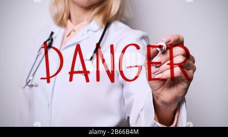 Femme medic écriture mot DANGER sur l'écran imaginaire contre fond blanc, closeup Banque D'Images