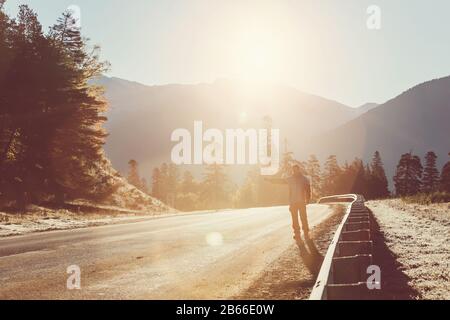 Homme Sur Vacances Hitchranking Le Long De Country Road Dans Les Montagnes. Sun Flare et filtre croisé ajoutés Banque D'Images