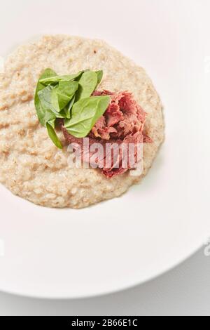 Vue rapprochée du porridge de flocons d'avoine avec du jambon à faible teneur en matières grasses et des épinards frais. Banque D'Images