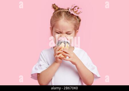 Jolie fille enfant avec plaisir mange de la glace savoureuse sur un fond de studio rose. Licks avec yeux fermés. Le concept de la nourriture de bébé et une enfance heureuse Banque D'Images