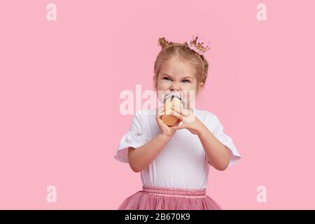 Jolie fille enfant avec plaisir mange de la glace savoureuse sur un fond de studio rose. Licks avec yeux fermés. Le concept de la nourriture de bébé et une enfance heureuse Banque D'Images