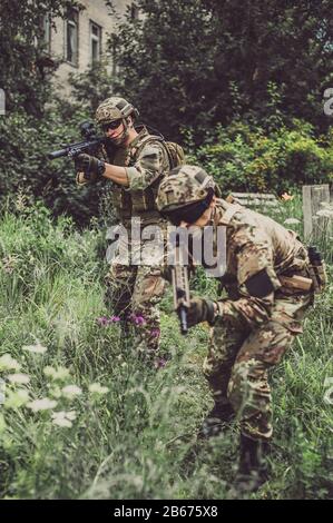 Deux hommes en uniformes militaires camouflage végétato avec fusils d'assaut automatiques avec visée optique et tir dans l'herbe haute dans la forêt Banque D'Images