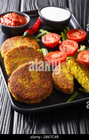 Falafel de style birman Baya Kyaw fait de petits pois jaunes avec légumes frais et sauces rapprochés dans une assiette sur la table. Vertical Banque D'Images