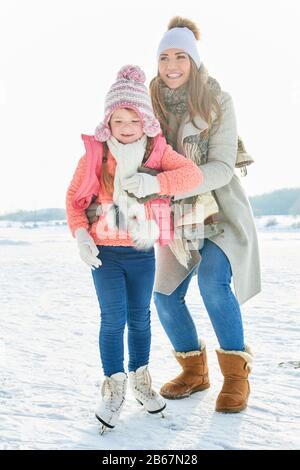 La mère aide l'enfant à apprendre à skate en hiver Banque D'Images