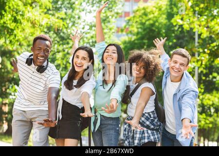 Portrait D'Étudiants Multiculturels Joyeux Se Posant Avec Des Mains Levées À L'Extérieur Banque D'Images