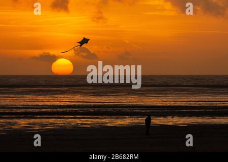 Un cerf-volant isolé avec queue est silhouetté volant au-dessus du soleil couchant alors qu'il s'enfonce dans la mer irlandaise à Lytham St annes Banque D'Images