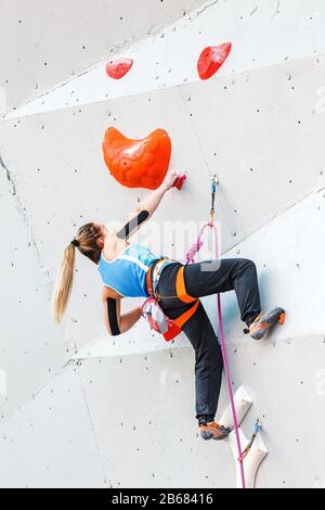 Une femme de sport musclée et ajustée fait de l'exercice dans le boulement et escalade à l'intérieur au mur artificiel avec bande Banque D'Images