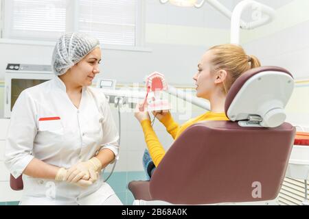 Un dentiste féminin traite les dents d'une patiente et explique comment la brosser correctement sur une mâchoire Banque D'Images