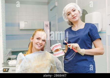 Jeune dentiste avec modèle de mâchoire et brosse explique l'hygiène et la santé de la bouche et des dents à son patient Banque D'Images