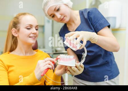 Jeune dentiste avec modèle de mâchoire et brosse explique l'hygiène et la santé de la bouche et des dents à son patient Banque D'Images