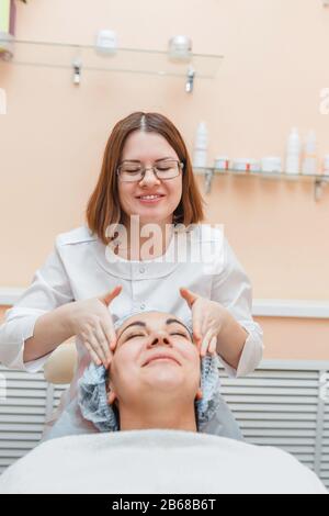 Une femme médecin dans une clinique de cosmologie massages et nettoie le visage du client en le préparant à la procédure de beauté Banque D'Images
