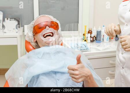 Patiente avec dilatateur dentaire dans sa bouche montrant le pouce vers le haut au cabinet du médecin Banque D'Images