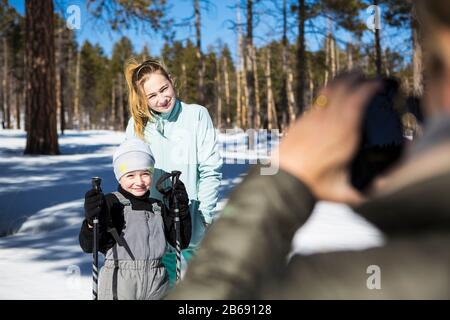 Mère prenant une photo de ses deux enfants, un garçon et une adolescente dans le paysage enneigé de la forêt. Banque D'Images