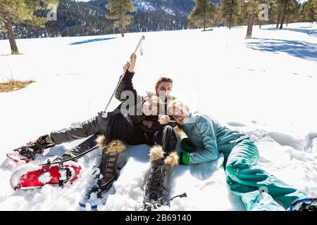 Une femme et ses deux enfants, une adolescente et un jeune garçon allongé dans la neige en chaussures de neige et équipement de ski. Banque D'Images