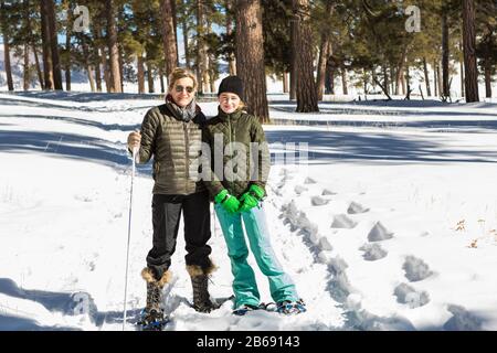 Une femme adulte et une adolescente en chaussures de neige dans les bois tenant des bâtons de ski Banque D'Images